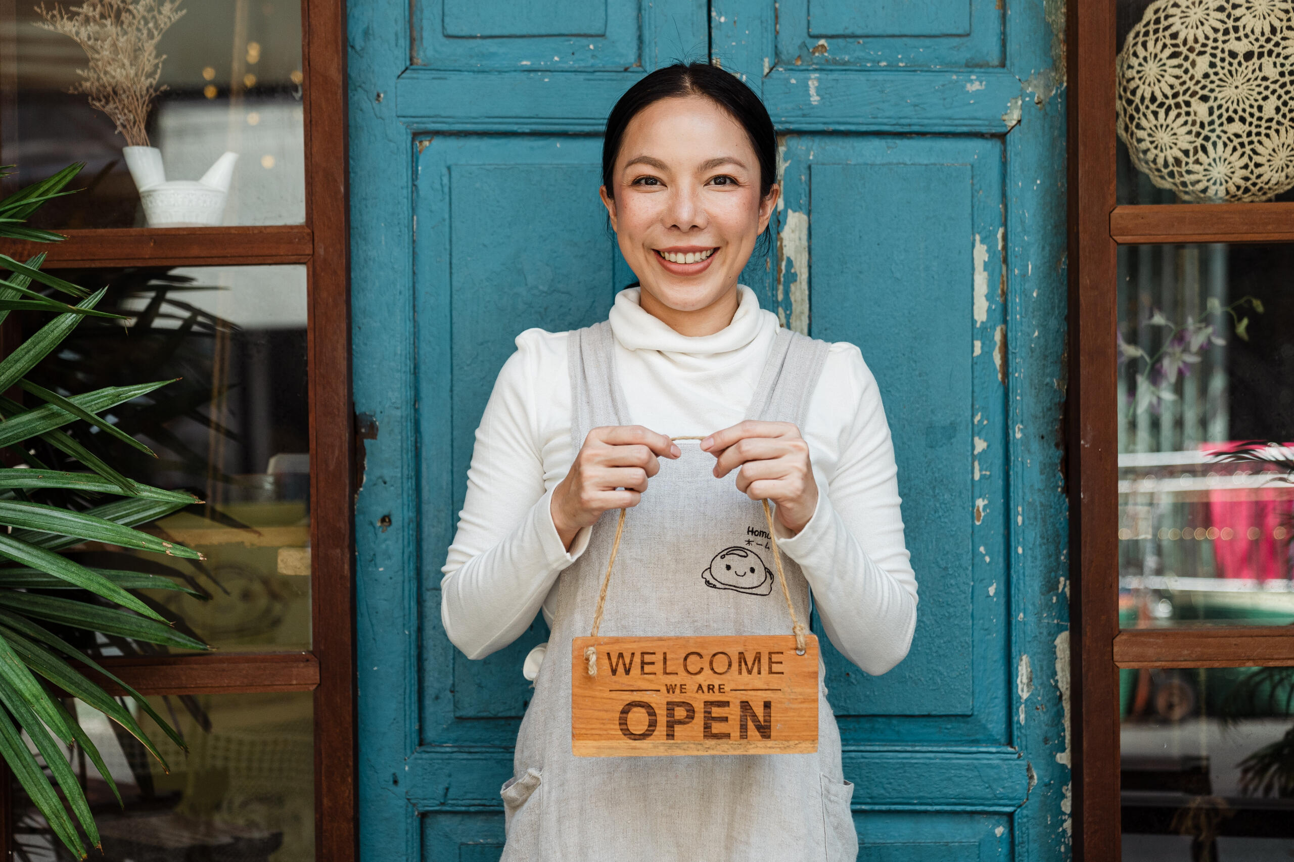 Ethnic female cafe owner showing welcome we are open inscription.